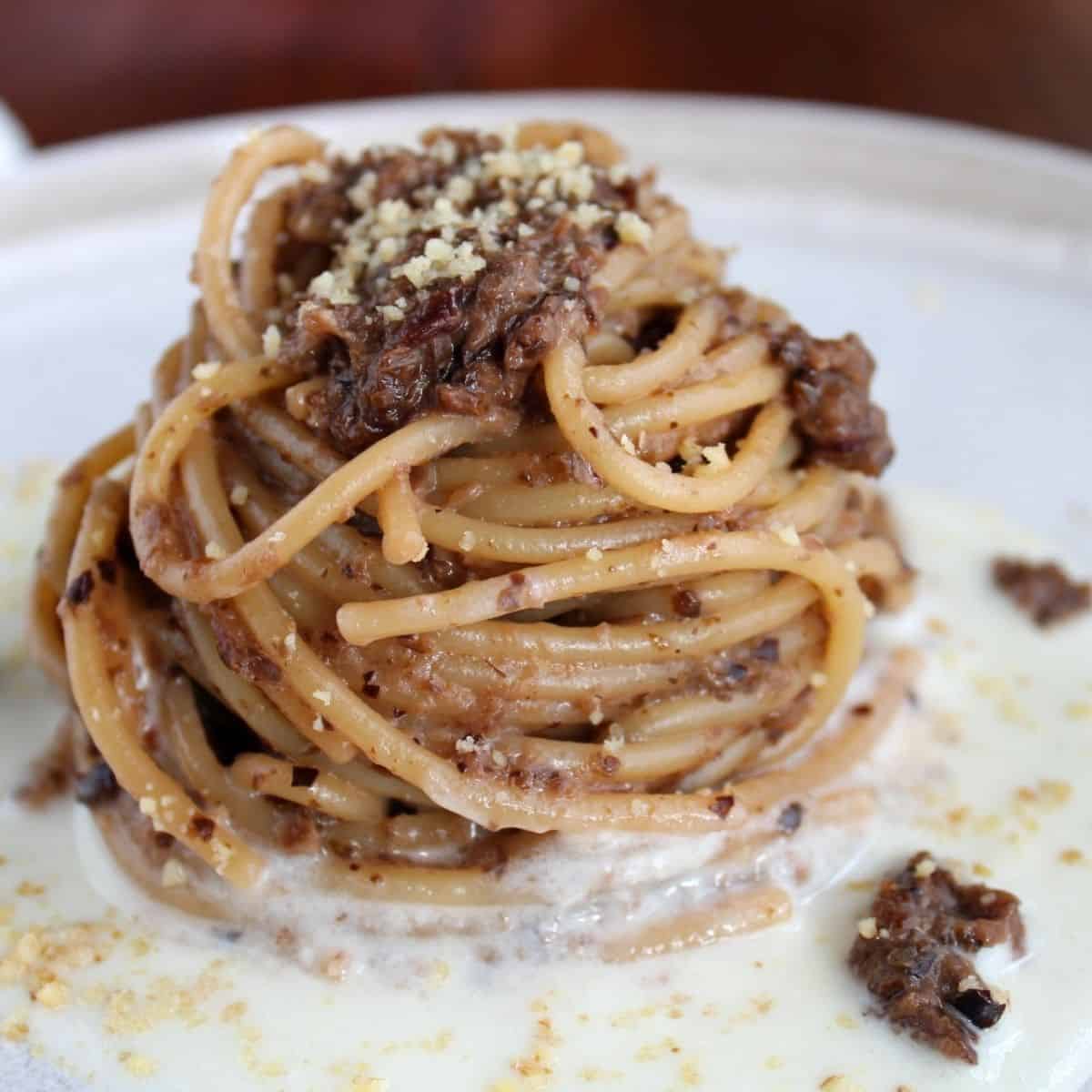 Spaghetti con radicchio Tardivo in un piatto bianco. La pasta poggia su uno strato di formaggio ed è condita con radicchio e gherigli di noci