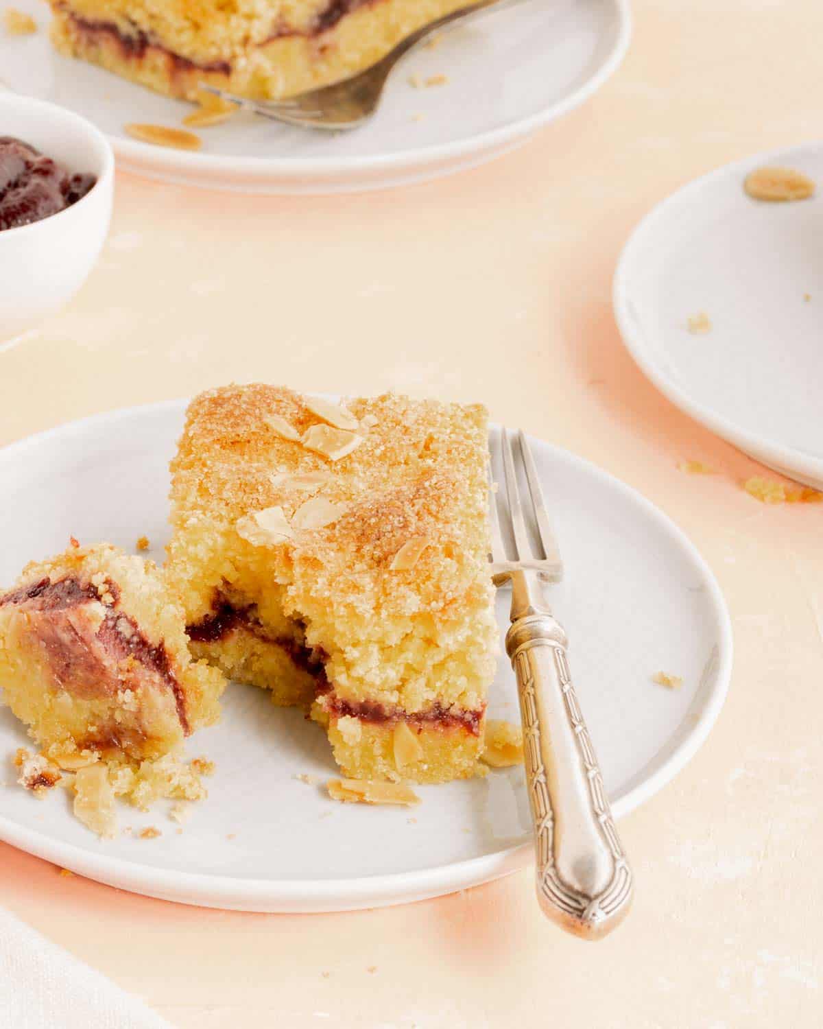 Primo piano di una fetta di Crostata Sabbiata con marmellata su un piatto bianco con una forchetta. La fetta mostra la marmellata all'interno della torta