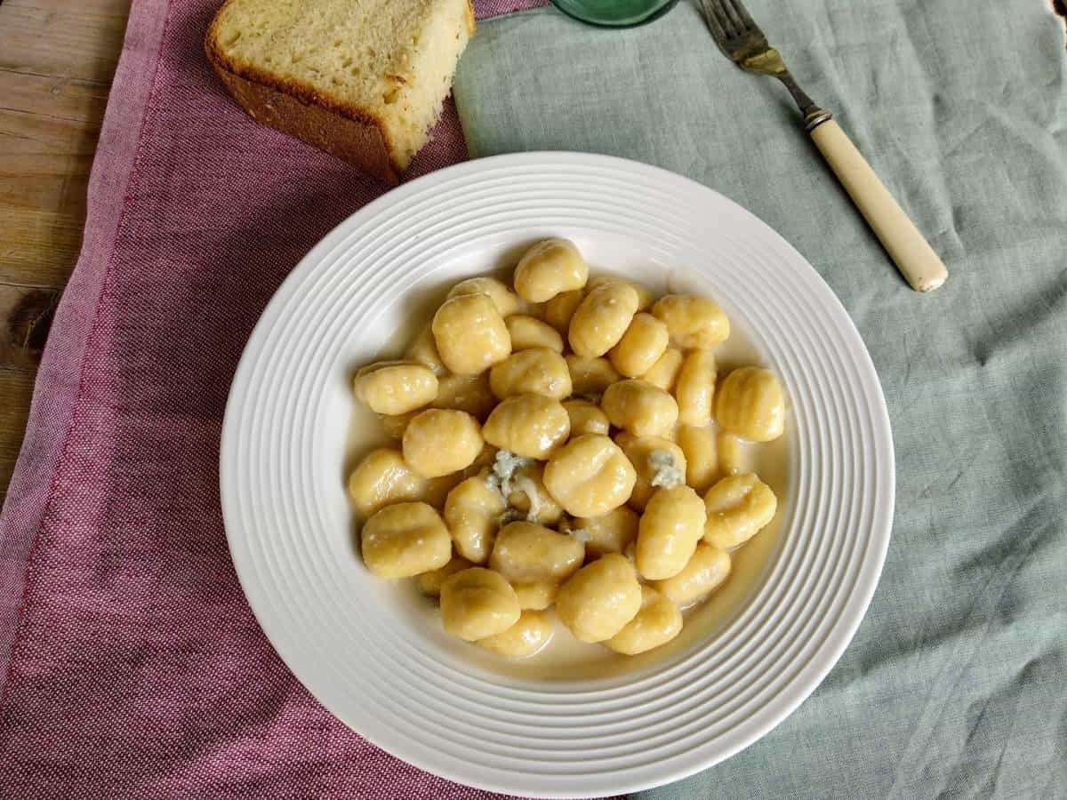Gnocchi al gorgonzola in un piatto bianco su lino verde e rosso e tavolo di legno. Il piatto mostra quanto sia cremoso il gorgonzola