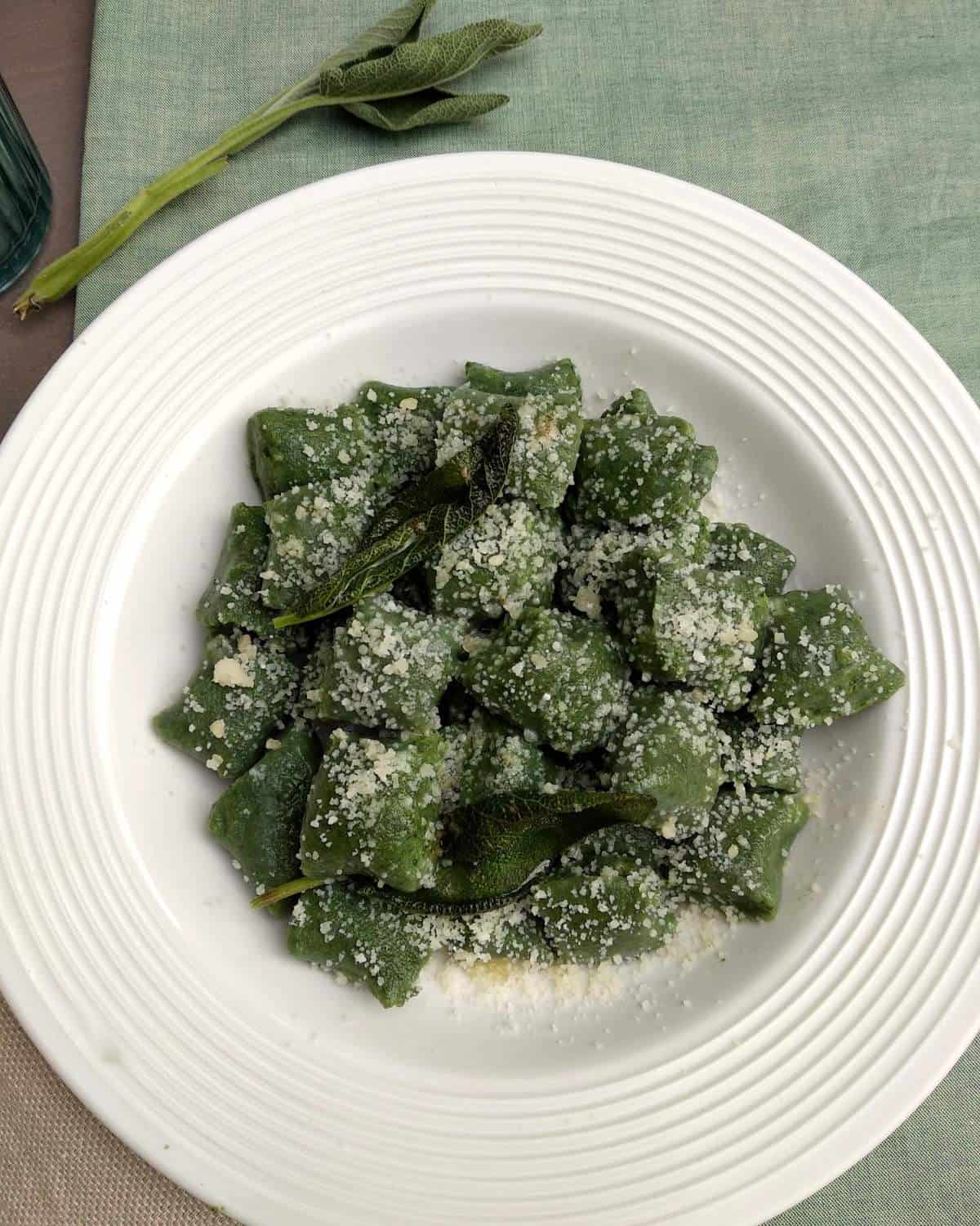 Gnocchi di ricotta e spinaci su un piatto bianco e lino verde. Gli gnocchi sono conditi con parmigiano grattugiato