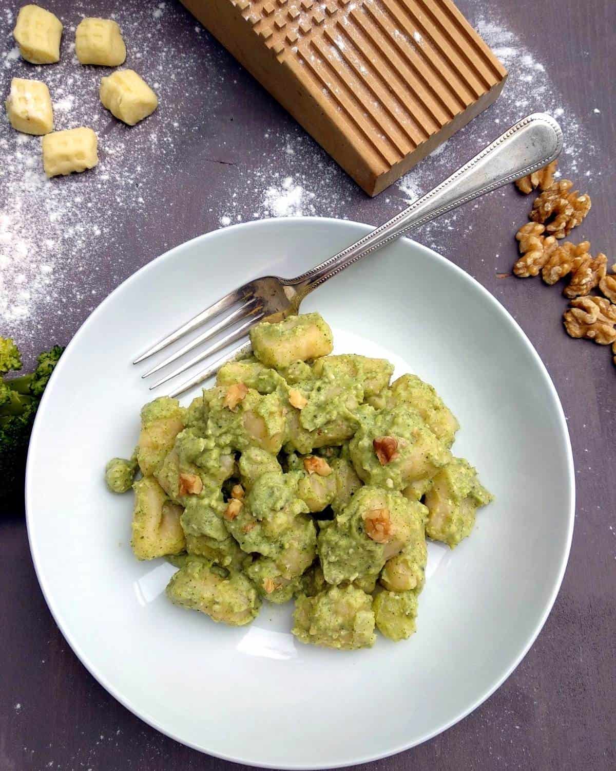 Gnocchi al Pesto di Broccoli in un piatto bianco con forchetta su tavolo di legno scuro. I gnocchi sono serviti con gherigli di noci.