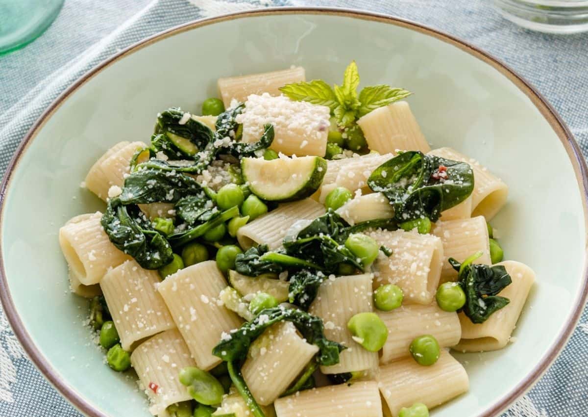 Una pasta di verdure verde su un piatto verde chiaro su tela blu. Il piatto mostra spinaci, piselli e zucchine