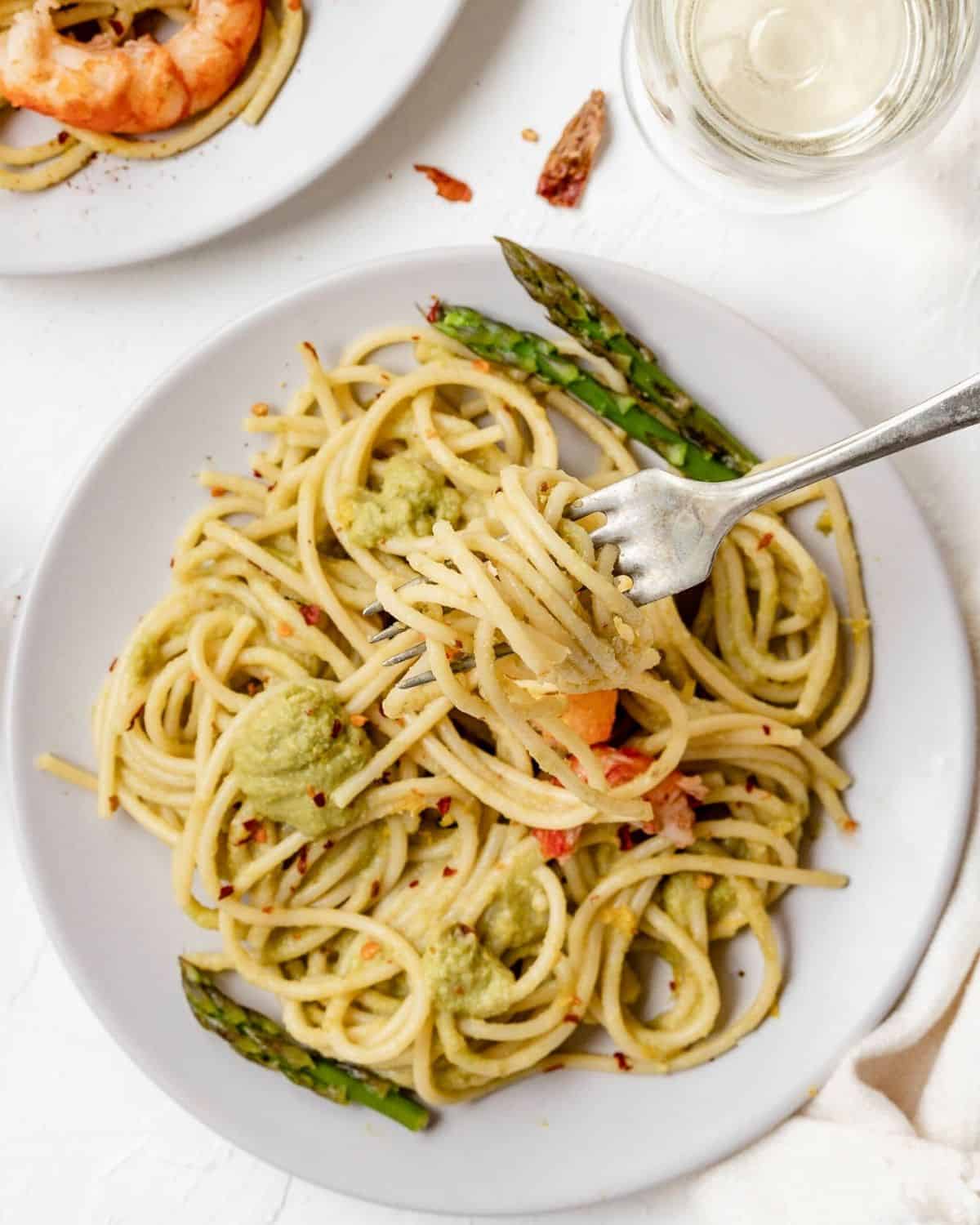 Una vista dall'alto Spaghetti agli asparagi con gamberi su una forchetta in un piatto bianco. È guarnito con asparagi.
