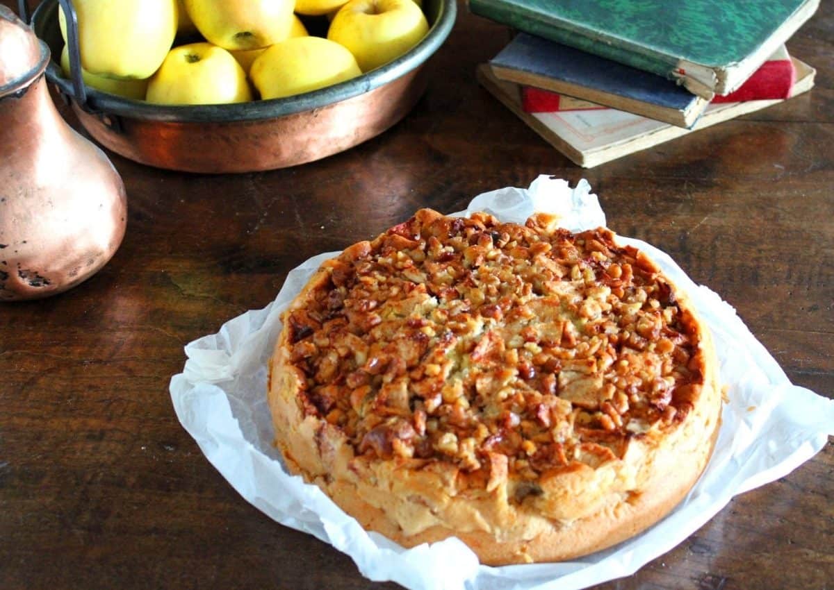 una vista a 45 gradi della torta di mele e noci su una carta forno su un tavolo di legno antico. Sullo sfondo mele e libri