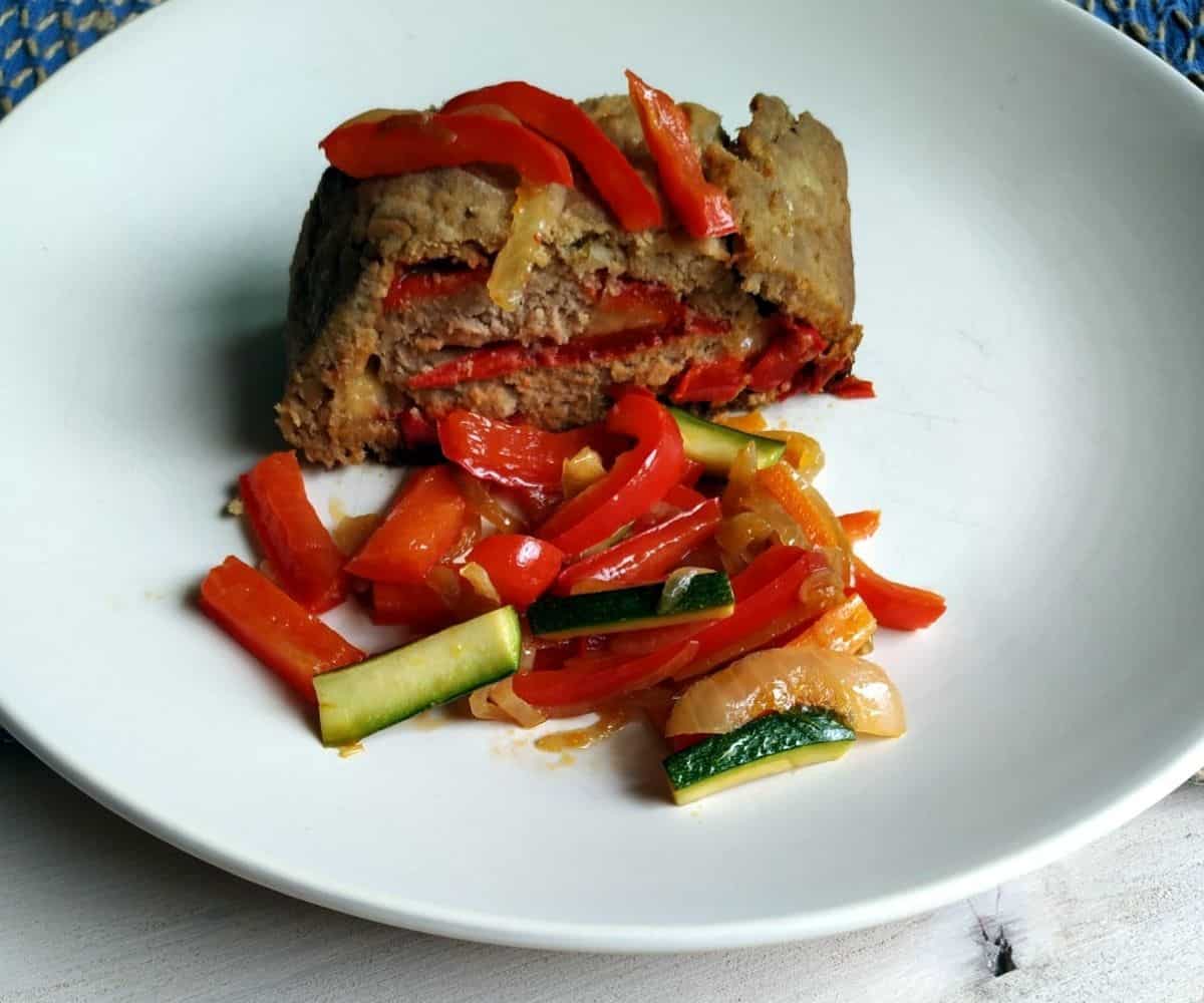 A slice of Peppers Meat Loaf on a white plate with some peppers as side dish.