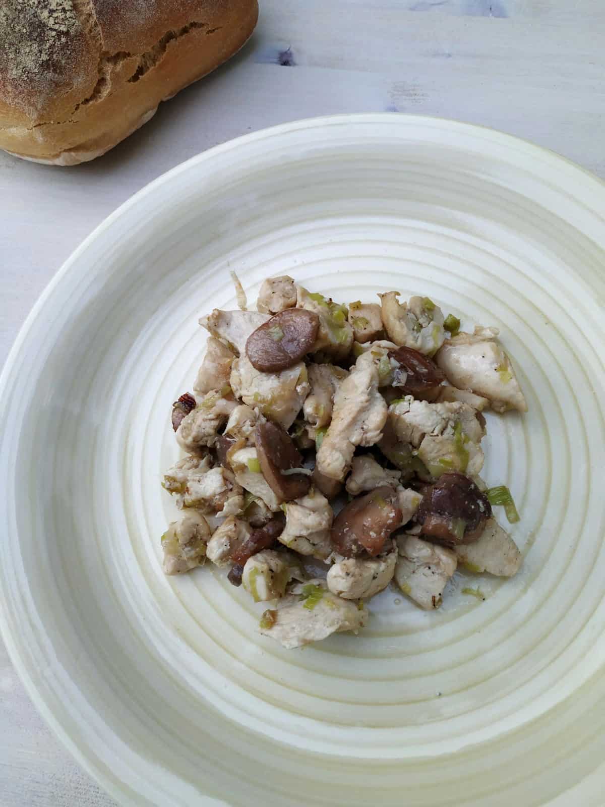 chicken with mushrooms on a white plate from above. It is topped with a few mushrooms