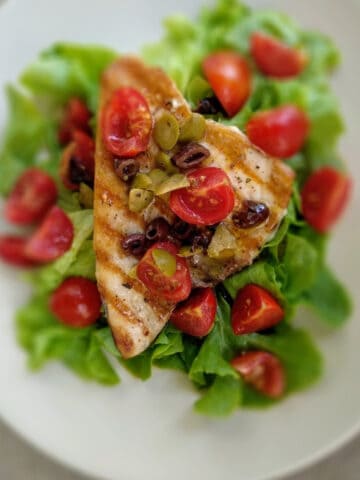 A Grilled-Swordfish on a white plate. It is garnished with chopped tomatoes and salad