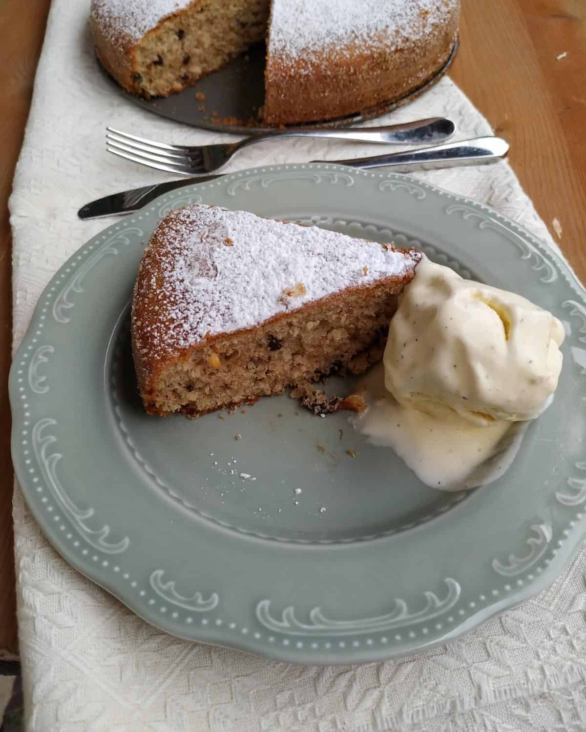 A slice of Hazelnuts Cake in a grey plate and white linen. The slice show the hazelnuts baked inside and the whipped cream on top
