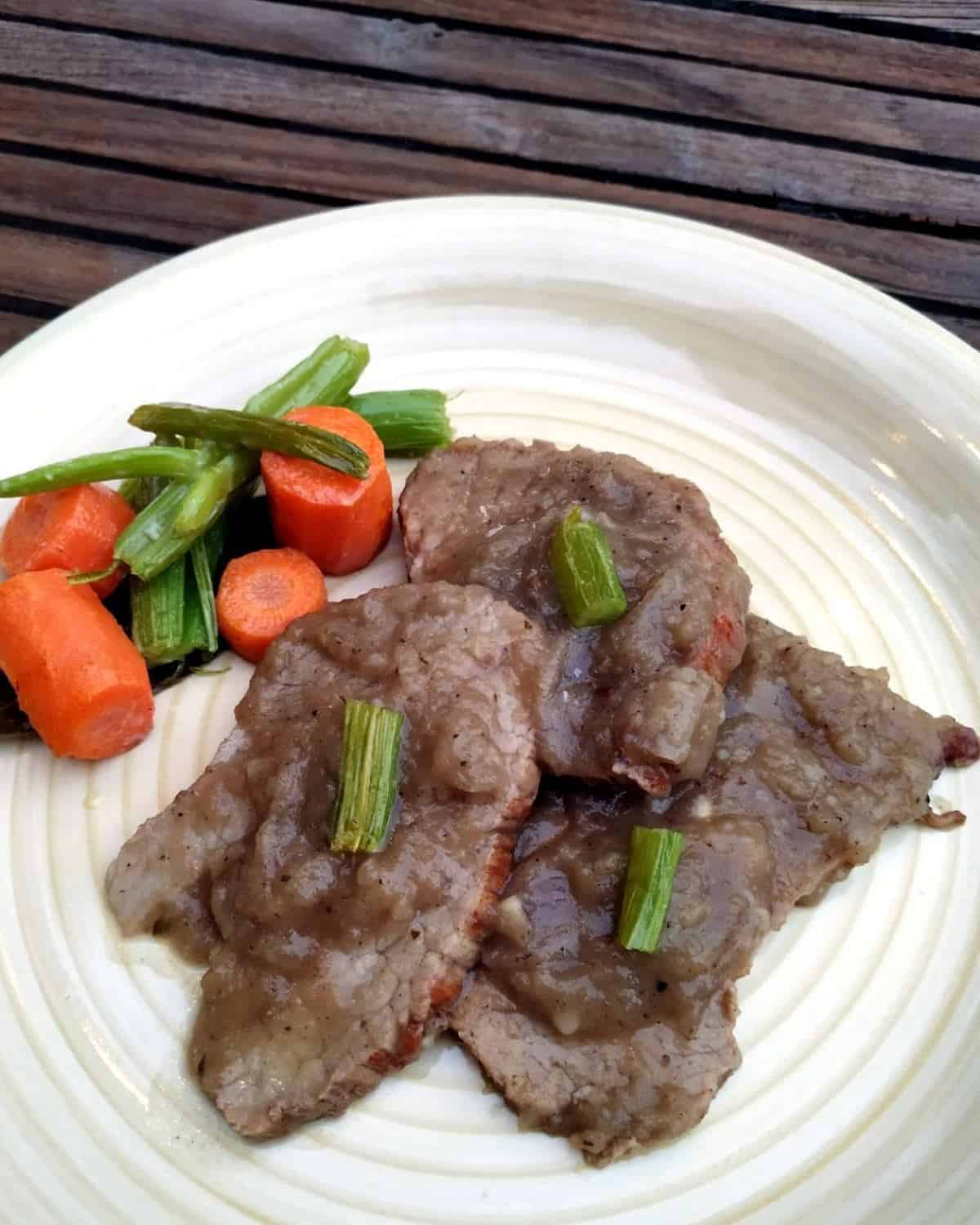 3 slices of Veal in Onion Sauce with some vegetables-on-a-white and yellow dish-