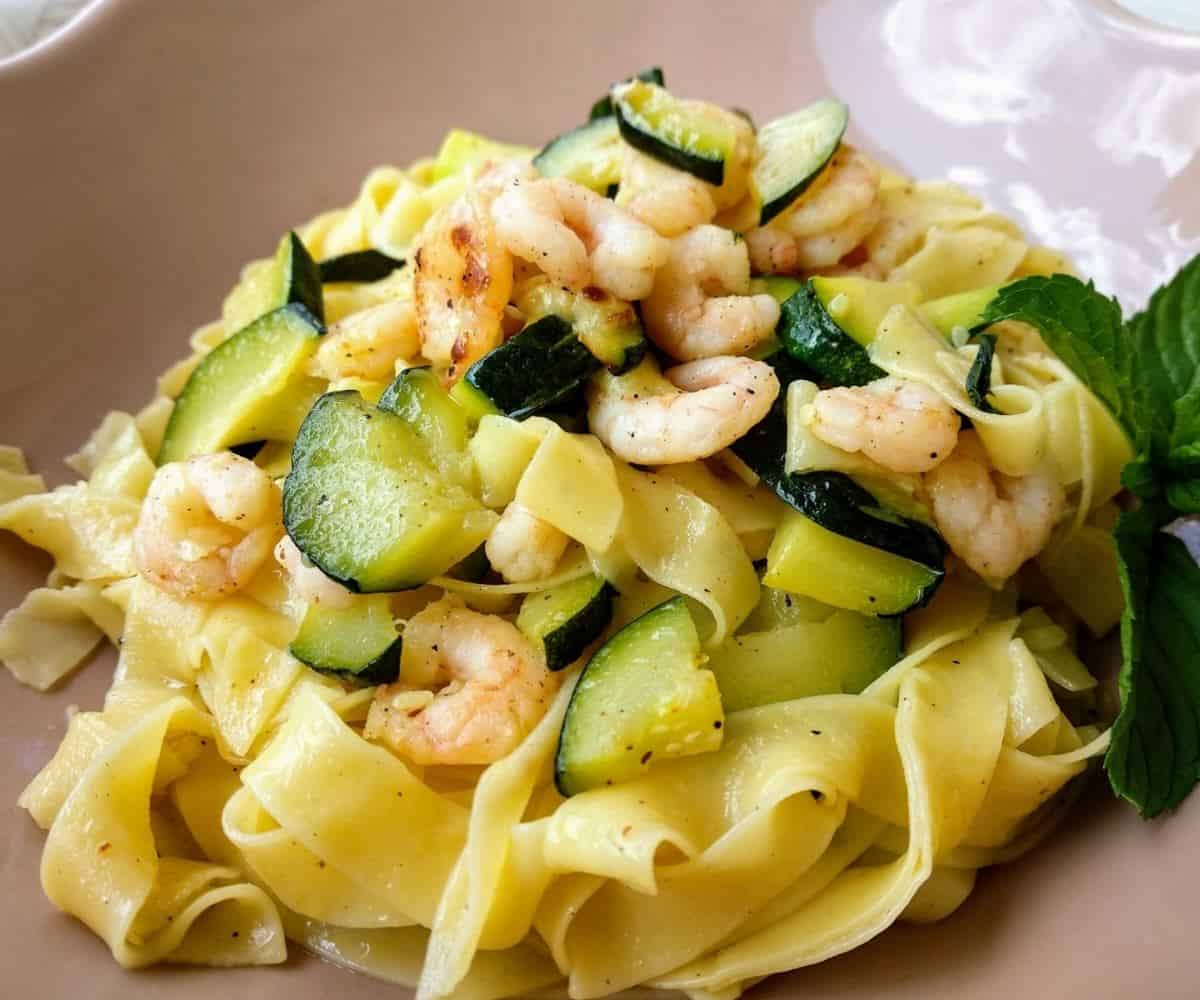 A close up of an Italian Tagliatelle with Praws and Zucchini in a light pink plate.