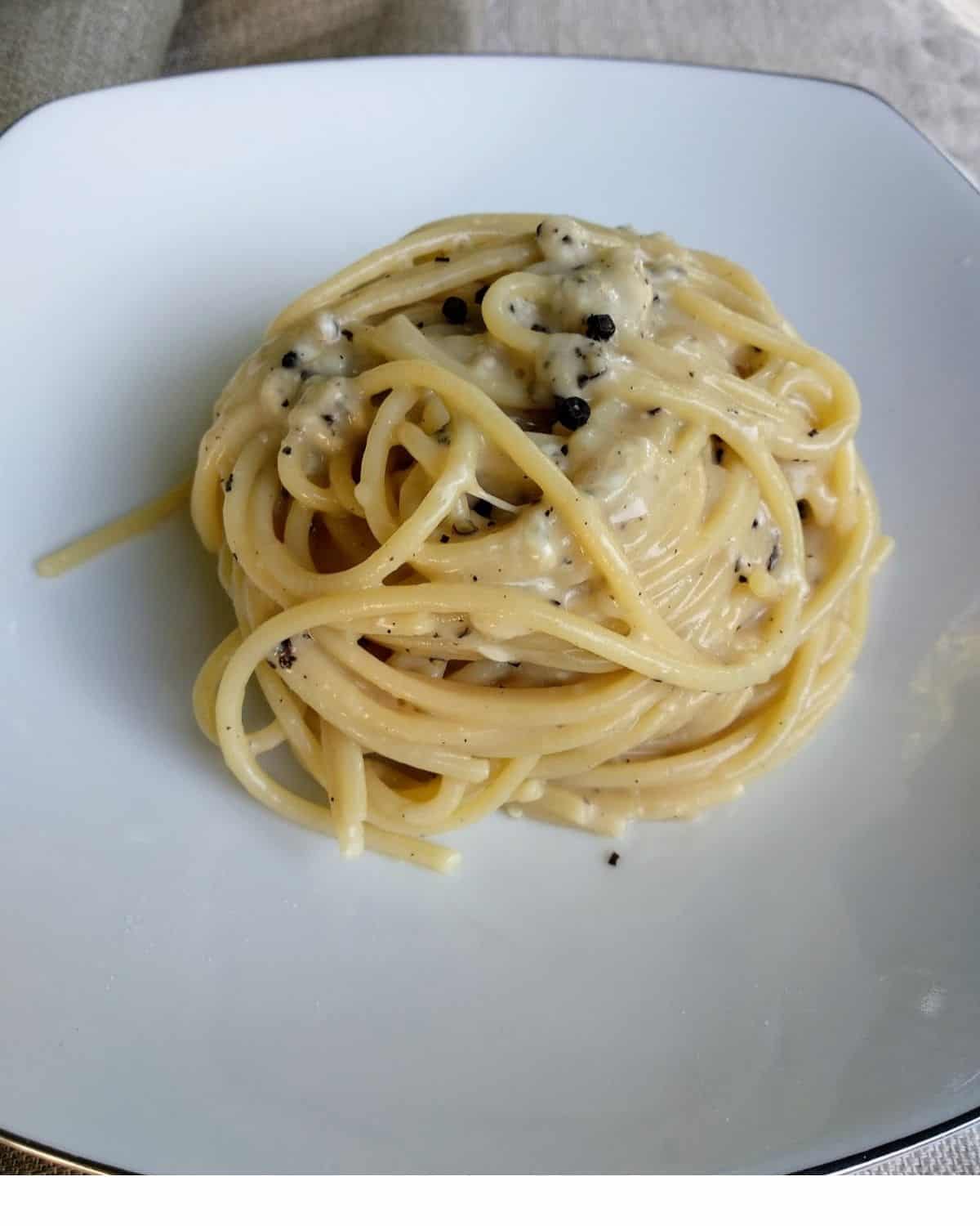 A view from above Cacio e Pepe Spaghetti in a white dish on a blue linen