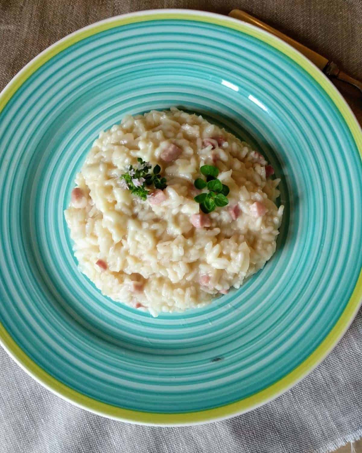 Cheesy-Risotto-with-Pancetta-Bancon on a blue/green dish and wooden table shown from above.