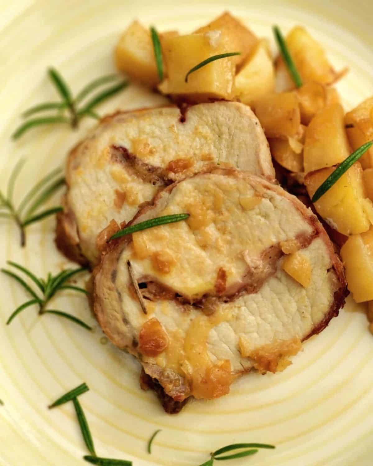 A close up of Aromatic Roasted Pork Roulade in a light dish with some roasted potatoes aside
