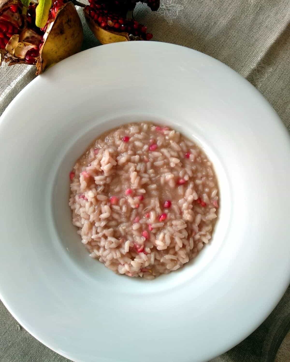 Pomegrate Risotto on a white plate shown from above. Risotto is topped with pomegrate