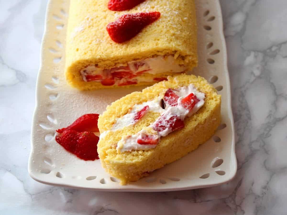 a close up photo of Strawberry And Ricotta Roll on a white plate showing the whipped cream ans strawberries inside the cake