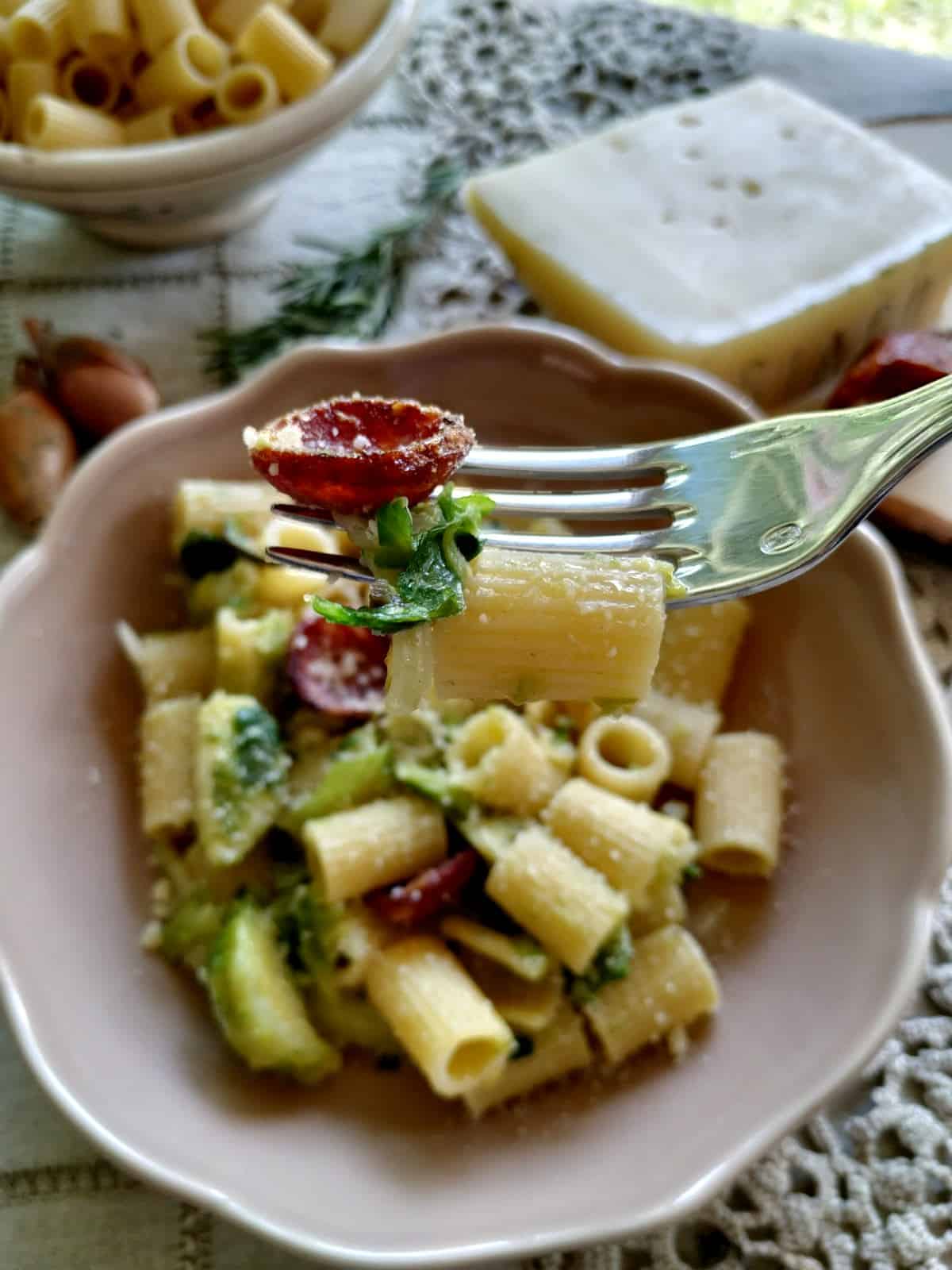 A close up from above of Brussels Sprouts Rigatoni on a soft pink plate. The pasta shown a fork with pasta and salami on it