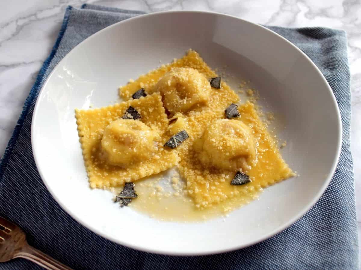 A view from above Potato and Speck Ravioloni in a white dish on a blue linen