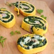 4 Slices of Frittata Roulade on a wooden board. The slices show the spinach, ham and cheese layers