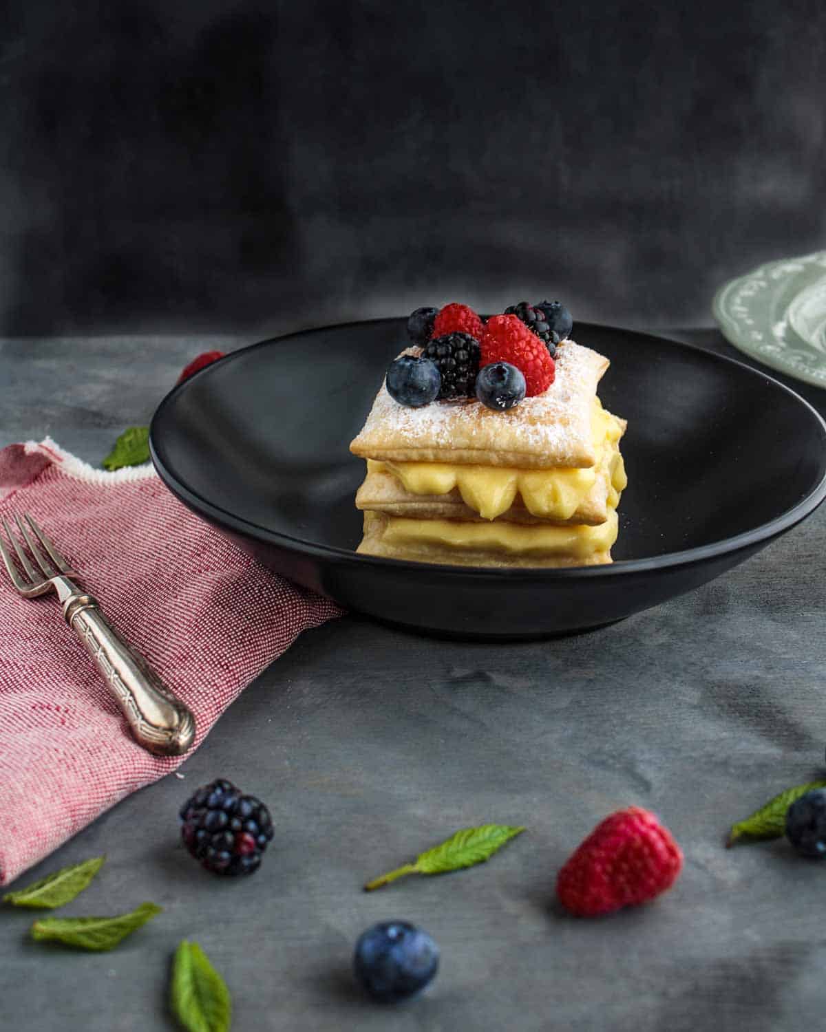 A slice of Millefoglie with Vanilla Custard and Wild Berries-on-a-black-dish-showing-the-custard-inside
