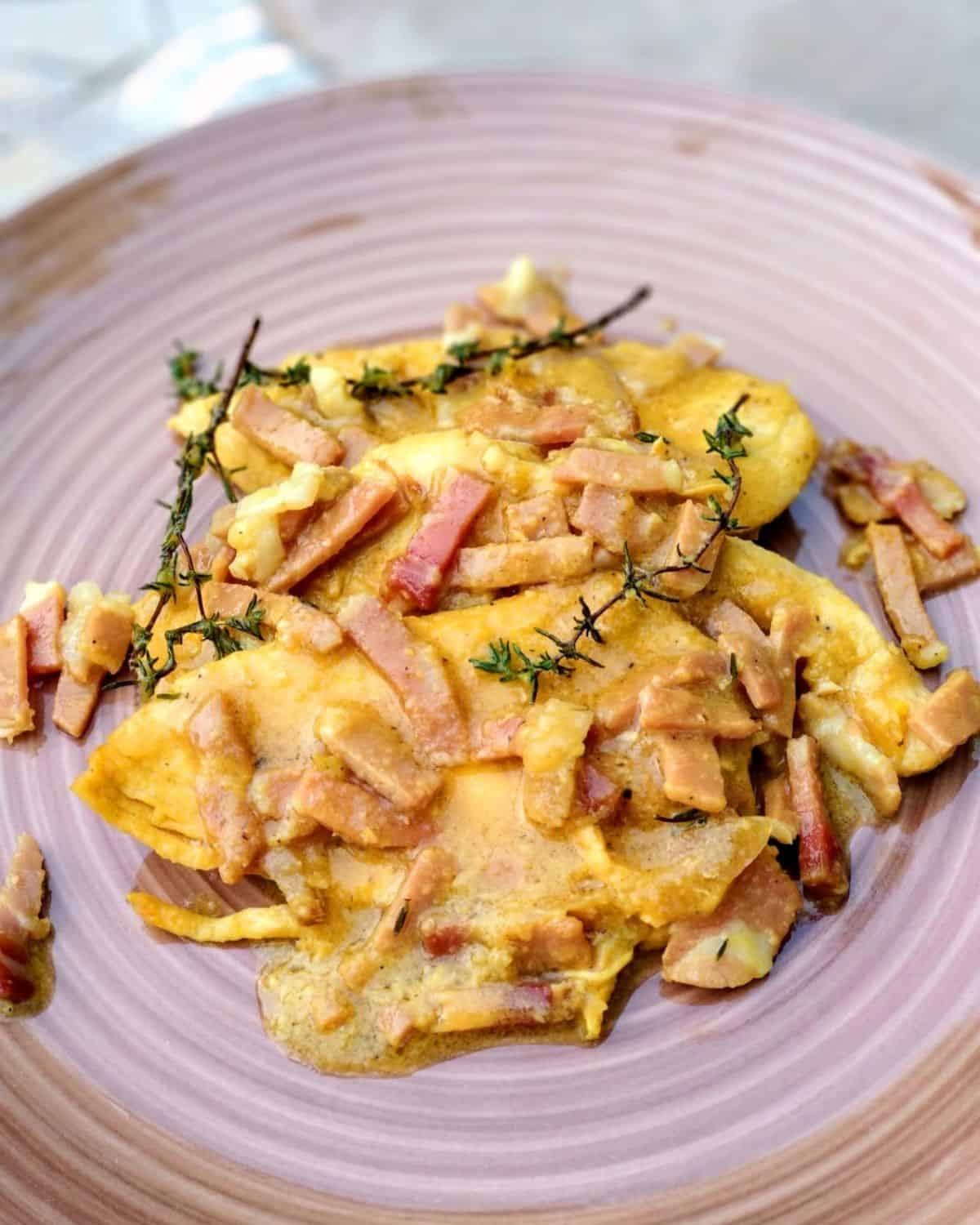 A close up from above of Saffron Chicken Breast with Speck on a light brown plate: The dish shown the saffron cream and some chopped speck on top of the chicken
