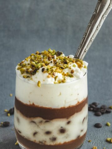 Chocolate Trifles with Custard in a glass with a spoon inside. It is topped with chopped pistachios