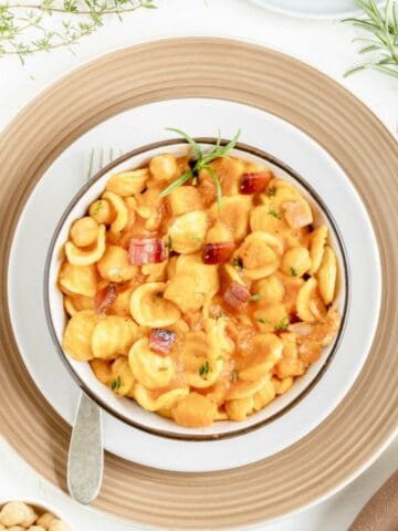 A view from above of a pasta bowl with a fork showing pasta with pumpkin, chickpeas, and speck