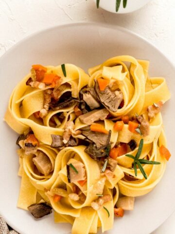 A close up from above of Mushrooms and Bacon Tagliatelle on a white plate. The pasta shown mushrooms and carrots on top