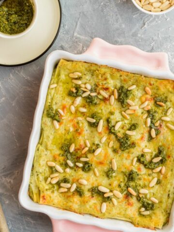 A view from above Pesto Lasagna in a pink pan. It is topped with pesto sauce and pine nuts