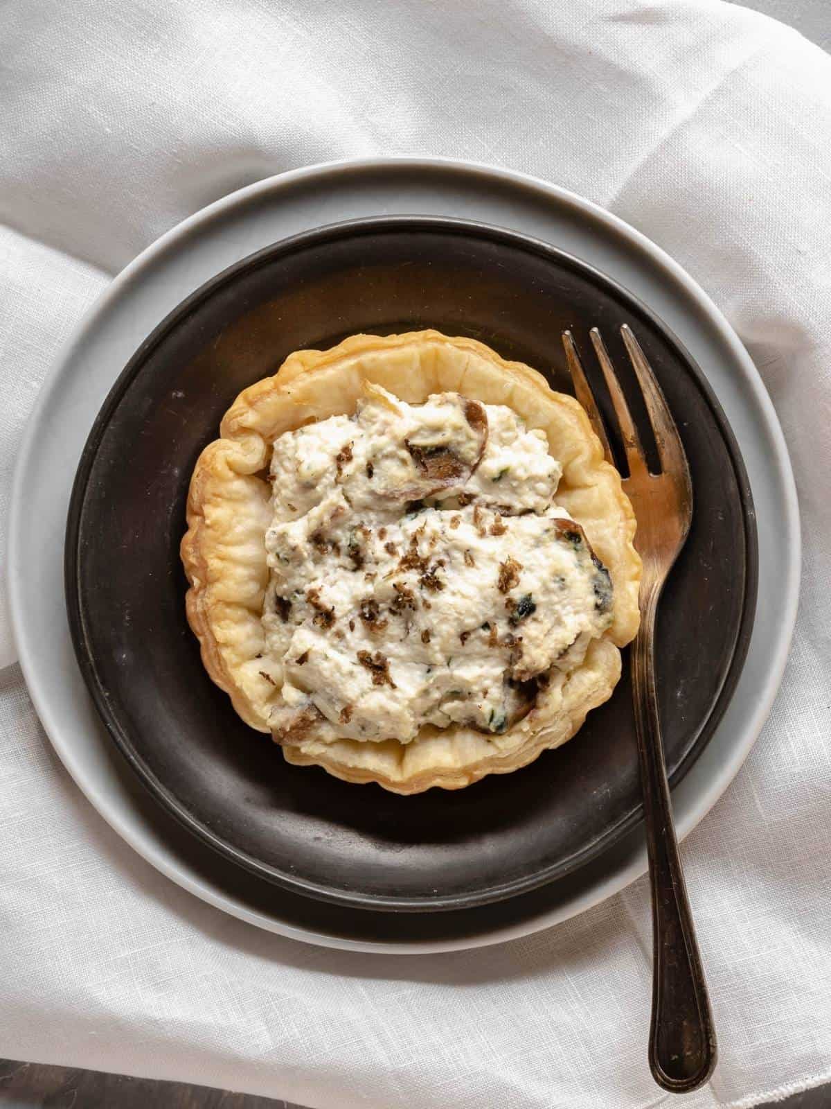 mini-puff-pastry-tart-ricotta-and-mushrooms-truffle-on-saucer-with-fork