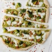 top view of pizza slices with broccoli and sausage on baking paper and white table. The pizza shows pieces of sausage and broccoli with which it is stuffed and the pepper flakes