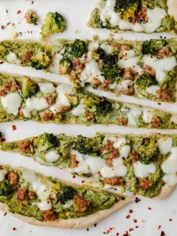top view of pizza slices with broccoli and sausage on baking paper and white table. The pizza shows pieces of sausage and broccoli with which it is stuffed and the pepper flakes