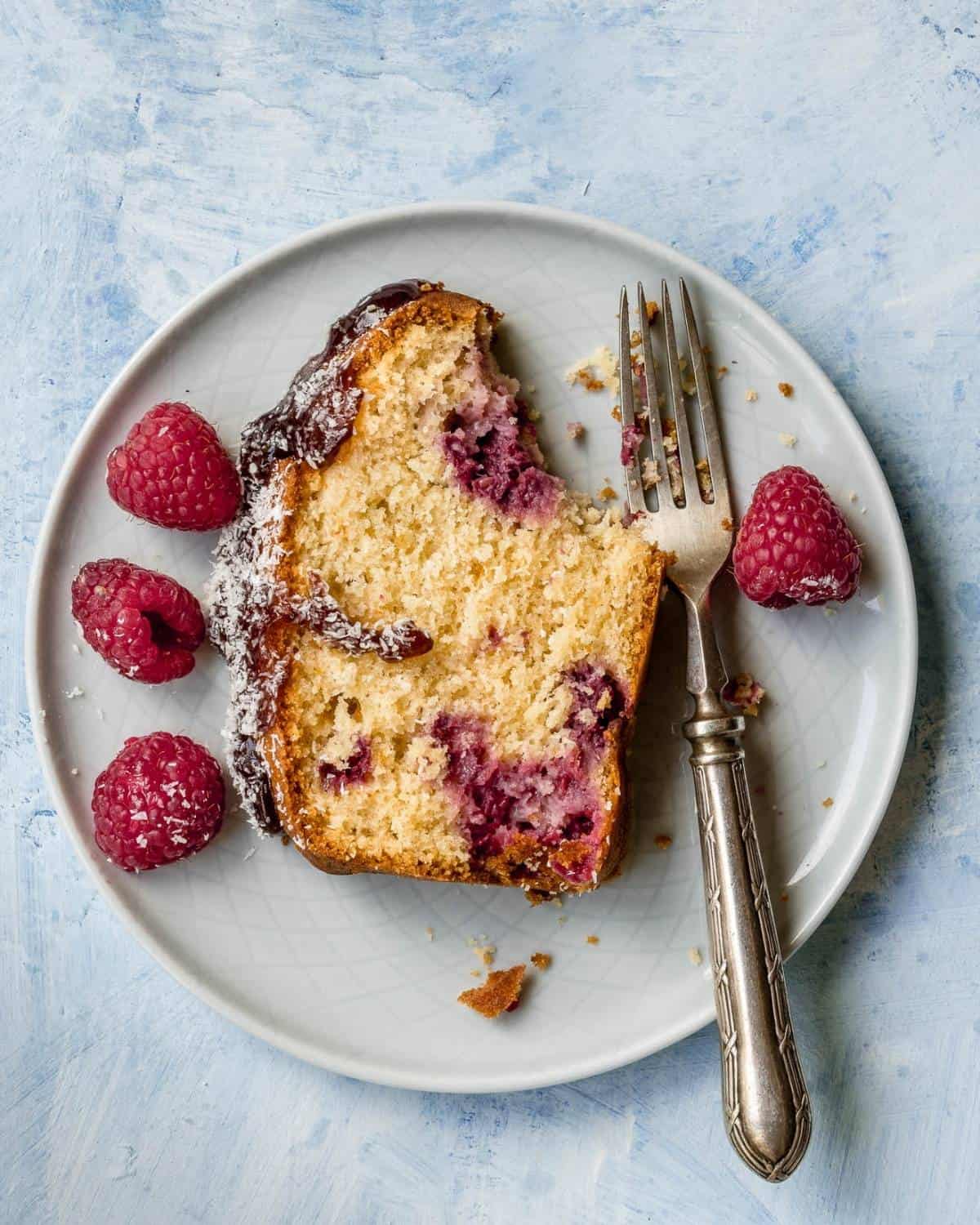 Slice-of-Coconut-and-Raspberry-Loaf-on-a-plate-with-a-fork-and-4-raspberries-aside
