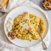 A view from above of Pumpkin Risotto with Gorgonzola in a white plate on a bright linen.It is topped with fresh parsley and walnuts