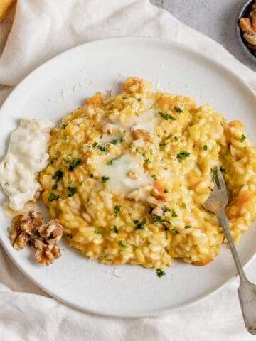 A view from above of Pumpkin Risotto with Gorgonzola in a white plate on a bright linen.It is topped with fresh parsley and walnuts