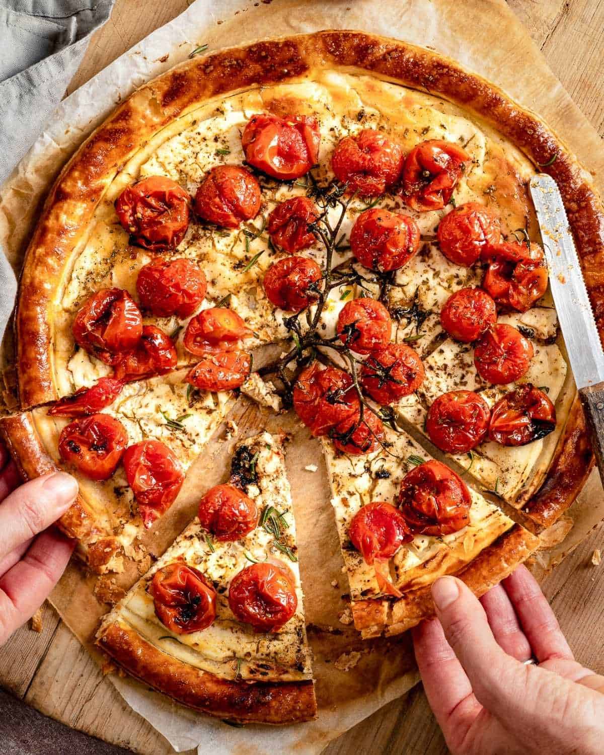 Two hands taking a slice of tomatoes tart