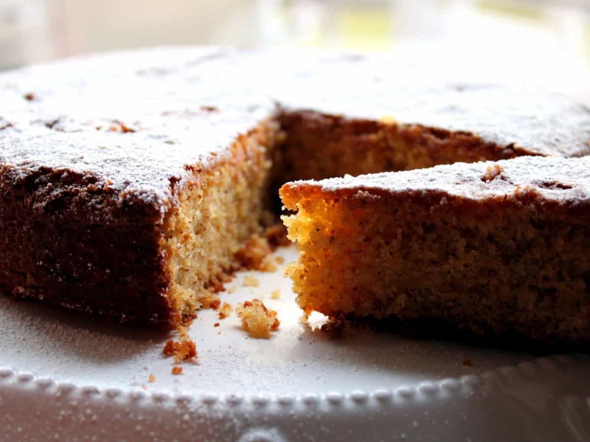 An almond Corn Cake on a white cake stand. The cake is sliced