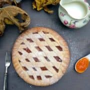 A close up shot from above of the Apricot Crostata showing the lattice with apricot jam. The tart is on a blue surface with a spoon full of jam on the right side and a fork opposite side