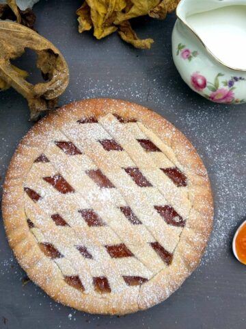 A close up shot from above of the Apricot Crostata showing the lattice with apricot jam. The tart is on a blue surface with a spoon full of jam on the right side and a fork opposite side