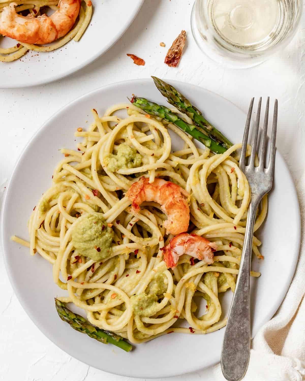 A view from above Asparagus Spaghetti with Prawns in a white dish with a fork. It is garnished with asparagus and prawns.