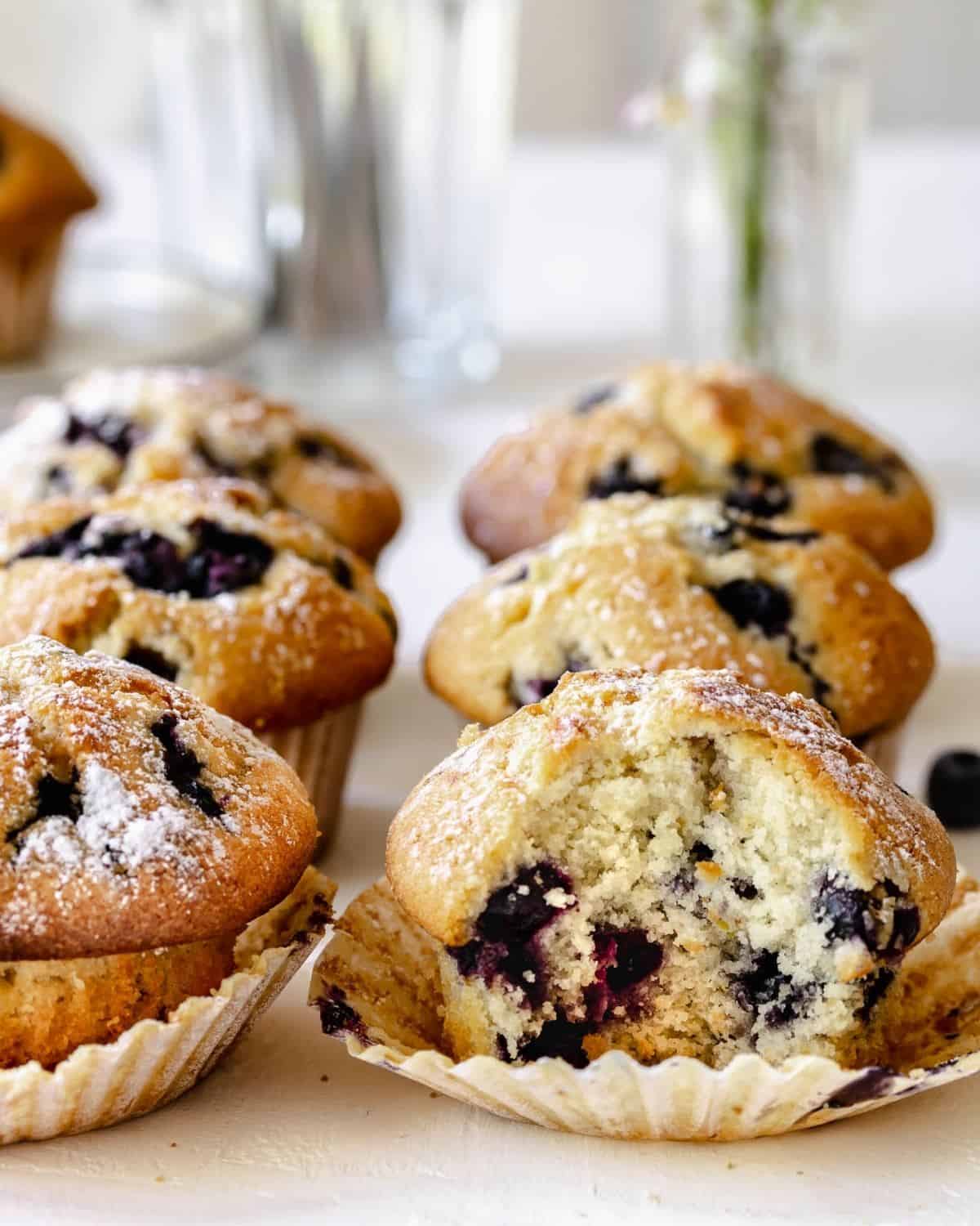 Front view of Blueberry Muffins. A muffin is open and blueberries can be seen inside