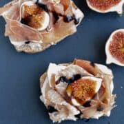 A close up from above of two Prosciutto crudo, gorgonzola and figs Italian Bruschetta. They have a quarter of fig and few drops of balsamic vinegar.on top