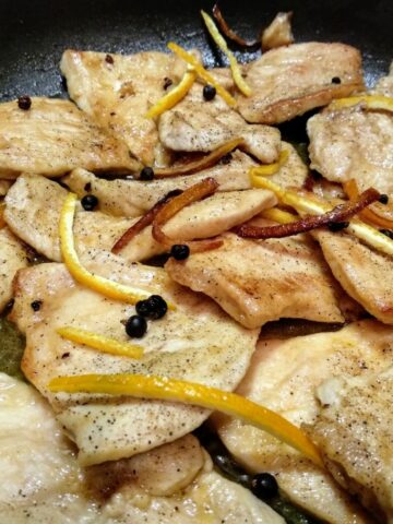 A close up from above of Chicken Breast slices with Juniper and Orange in a pan.