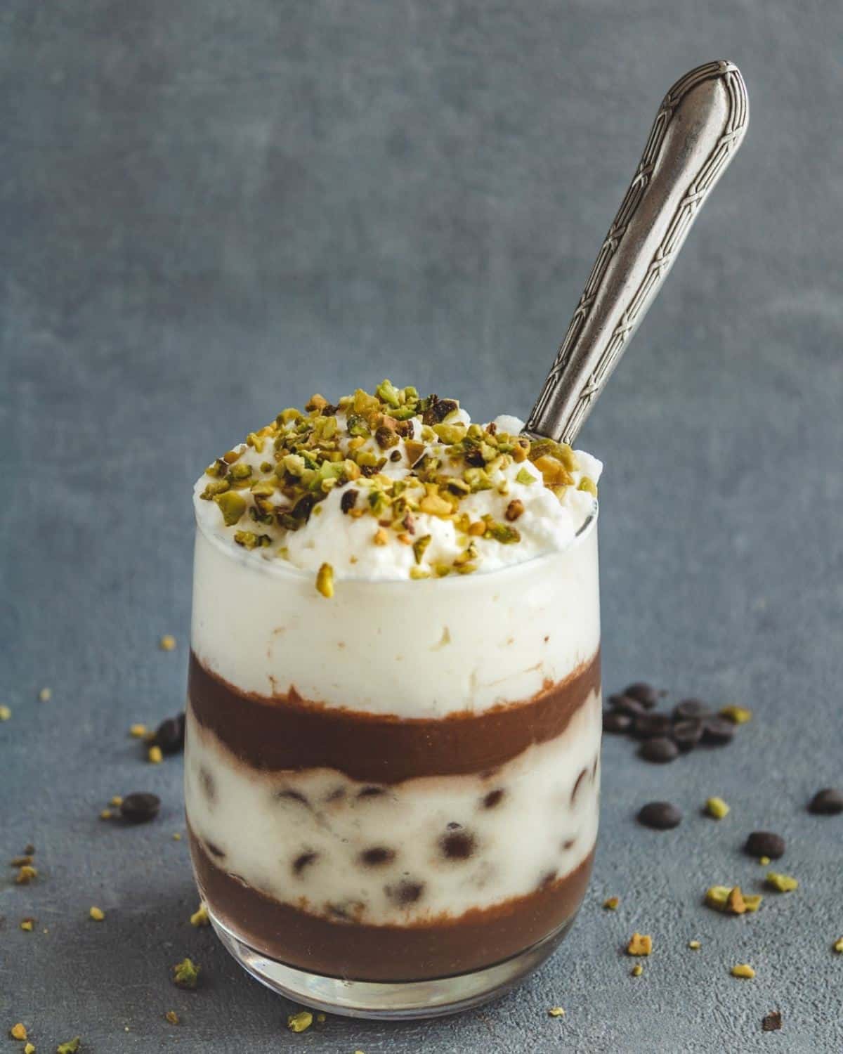 Chocolate Triles with Custard in a glass with a spoon inside. It is topped with chopped pistachios 