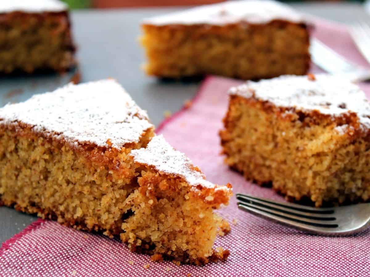 A few slices of Corn Cake on a red linene and wooden table. Slices are topped with icing sugar