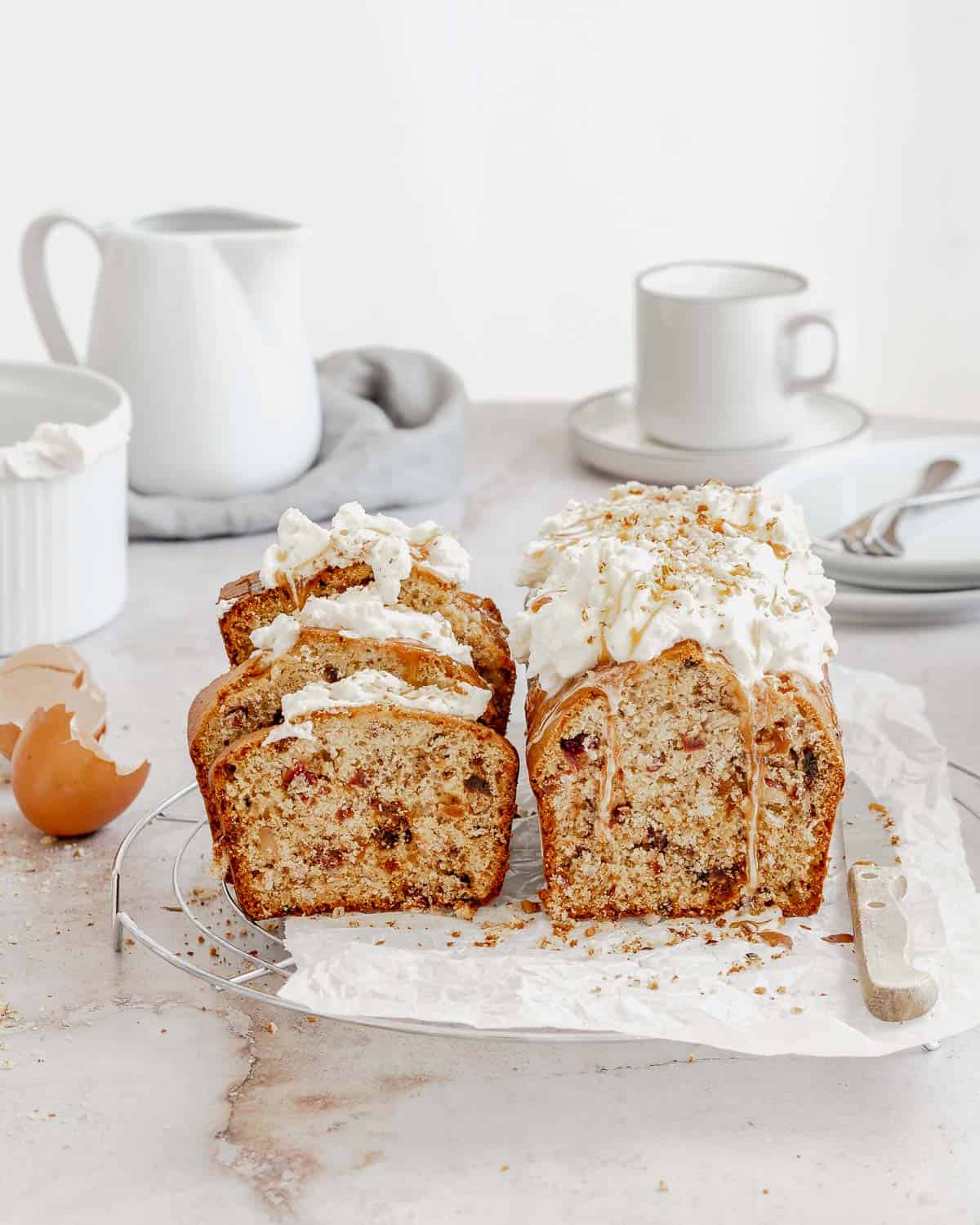 A-Dried Fruits Loaf with Walnuts and Almonds-on-a-tray-with-parchment-paper-the-loaf-has-fresh-whipped-cream-and-caramel-on-top- it-is-sliced-showing-the-dired-fruits-inside-