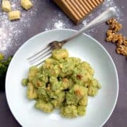 Broccoli Pesto Gnocchi in white plate with fork on dark wooden table. Gnocchi are served with walnut kernels.