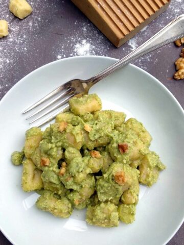 Broccoli Pesto Gnocchi in white plate with fork on dark wooden table. Gnocchi are served with walnut kernels.