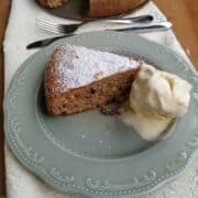 A slice of Hazelnuts Cake in a grey plate and white linen. The slice show the hazelnuts baked inside and the whipped cream on top
