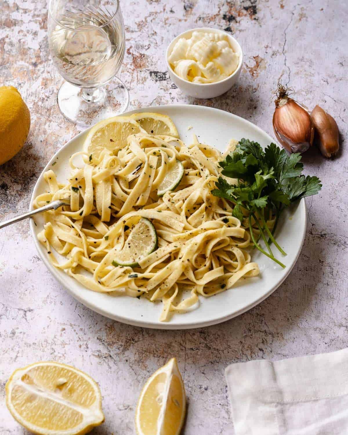 Lemon Tagliatelle in a white plate with a fork. The pasta is garnished with fresh parsley and sliced lemons