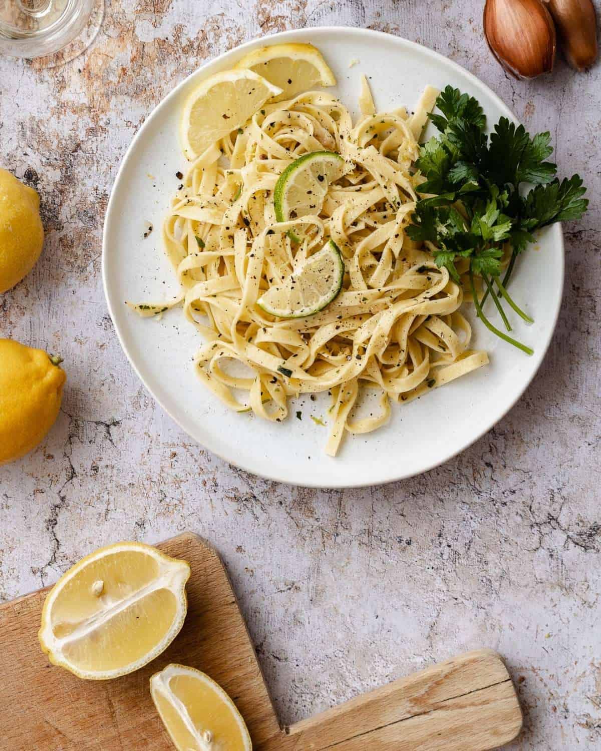 A view from above Lemon Tagliatelle in a white dish on a marble table. The dish is garnished with fresh parsley. On the side a sliced lemon on a wooden board